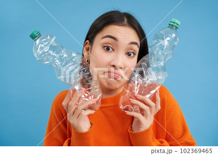 Thoughtful korean woman shows two plastic bottles, looks clueless and puzzled, concept of recycling and ecology Thoughtful korean woman shows two plastic bottles, looks clueless and puzzled, concept of recycling and ecology 102369465