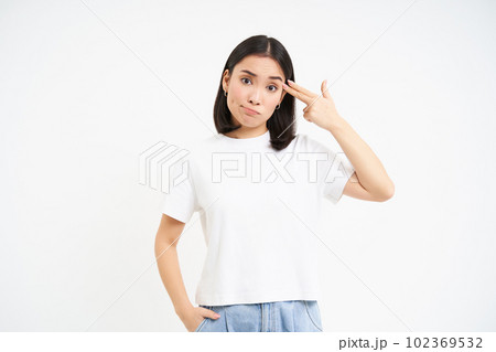 Annoyed asian woman, student shows finger pistol near head, looks bothered and tired, stands isolated on white background 102369532