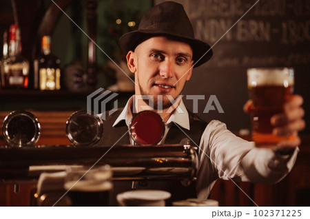 bartender serves in hand a glass of light draft beer lager with foam at bar counter bartender serves in hand a glass of light draft beer lager with foam at bar counter 102371225