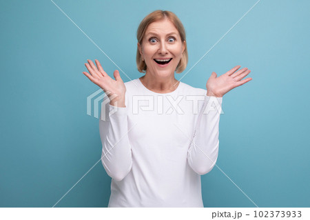 blond 50s woman in a white sweater reports the news on a studio background with copy space 102373933