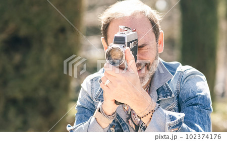 Mature man shooting video in city park with vintage camera Mature man shooting video in city park with vintage camera 102374176