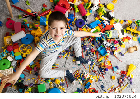 A little boy sits among scattered toys and smiles looking into the camera 102375914