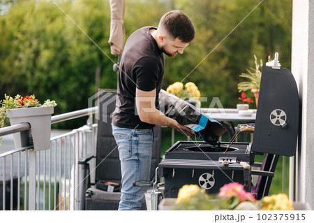 Man pours out charcoal into BBQ grill on terrace. Male preparing for backyard barbecue  102375915