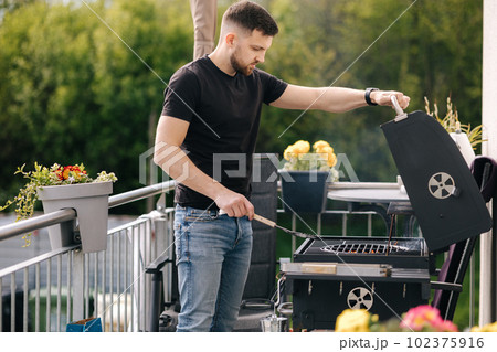 Side view of man open BBQ to see how the fire burns. Preparing for summer party 102375916