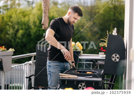 Handsome man make a fire and controls the process. BBQ grill outdoor 102375939