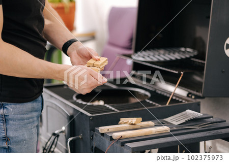 Close-up of man use fire briquettes for lighting a fire in the grill. Outdoor barbecue on terrace 102375973