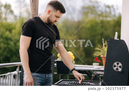 Handsome man cleaning BBQ grill to make some steak. Male use napkin to clean the grill of grease Handsome man cleaning BBQ grill to make some steak. Male use napkin to clean the grill of grease 102375977