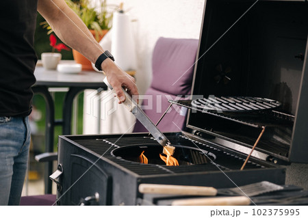 Close-up of man make a fire and controls the process. BBQ grill outdoor 102375995