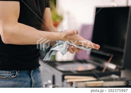 Close-up of male using towel to wipe dirt from hands while the fire is burning in the grill 102375997