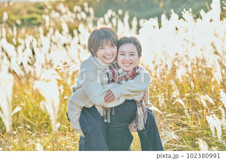 ススキを背景に友達をおんぶする仲良しの若い女性と友達 102380991