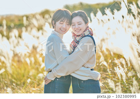 ススキを背景に抱き合う若い女性と友達 ススキを背景に抱き合う若い女性と友達 102380995