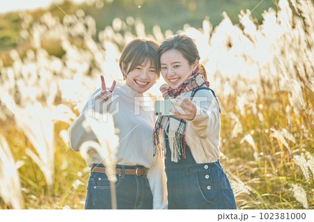ススキを背景にスマホで写真を撮る若い女性と友達 102381000