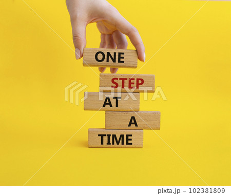 One step at a time symbol. Concept words One step at a time on wooden blocks. Beautiful yellow background. Businessman hand. Business and One step at a time concept. Copy space. One step at a time symbol. Concept words One step at a time on wooden blocks. Beautiful yellow background. Businessman hand. Business and One step at a time concept. Copy space. 102381809