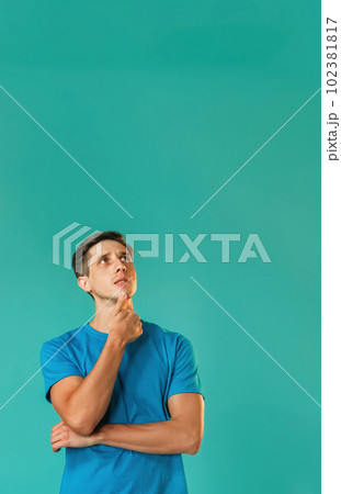 Puzzled man. Information background. Handsome thoughtful pensive guy in blue remembering holding chin looking up isolated on turquoise empty space. 102381817