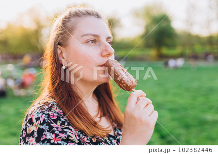 Happy young woman with delicious chocolate ice cream outdoors. Unhealhty food and weight loss concept. Summer time, eating 102382446