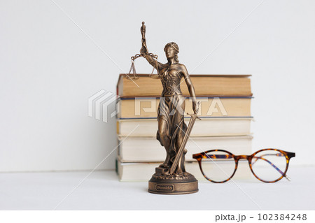 Themis goddess of justice statuette on light background on table with books and glasses. Themis goddess of justice statuette on light background on table with books and glasses. 102384248
