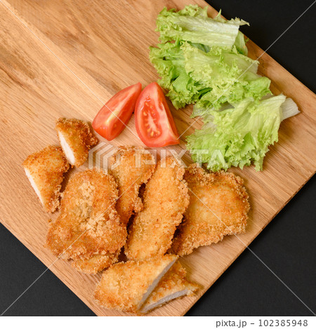 Chicken nuggets on a wooden board on a black background Chicken nuggets on a wooden board on a black background 102385948