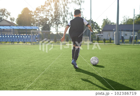 A young man in a black sports uniform trains in a football game at a stadium with artificial grass 102386719
