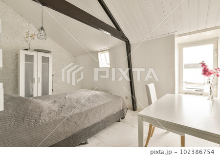 a bedroom with a bed, table and chair next to a window that has white paint on the wall behind it a bedroom with a bed, table and chair next to a window that has white paint on the wall behind it 102386754
