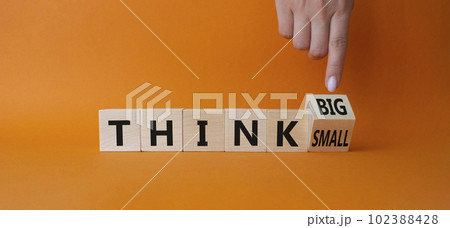 Think Big vs Small symbol. Businessman Hand points at wooden cubes with words Think Small and Think Big. Beautiful orange background. Business and Think concept. Copy space 102388428