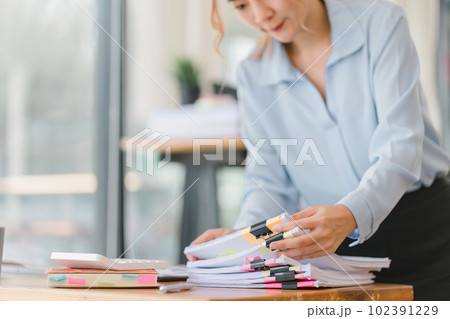 A businesswoman is sifting through stacks of paper files and folders that contain both incomplete and completed documents. Selective focus 102391229