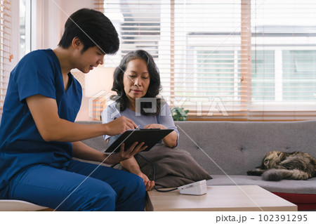 Young Asian male nurse, assisted living in-home carer, or doctor visiting an old senior citizen at home to talk about result follow-up checklist, healthcare advice, or prescription. 102391295