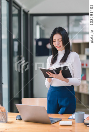 Portrait of a successful and lovely millennial Asian businesswoman, secretary, sales manager, or business consultant, sitting at her workplace with a laptop, smiling, while dressed casually. Portrait of a successful and lovely millennial Asian businesswoman, secretary, sales manager, or business consultant, sitting at her workplace with a laptop, smiling, while dressed casually. 102391403