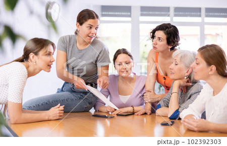 Women discuss documents sitting at table in office Women discuss documents sitting at table in office 102392303