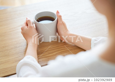 マグカップを抱えて考え込む女性の手元 102392989