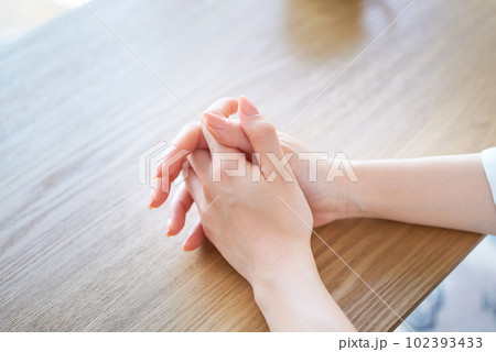 手を組んで考え込む女性の手元 102393433