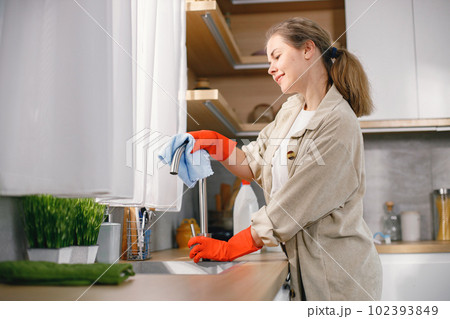 Portrait of a woman cleaning in a kitchen and wearing red gloves. Caucasian woman doing housework. Woman holding a rug and wiping a tape. 102393849