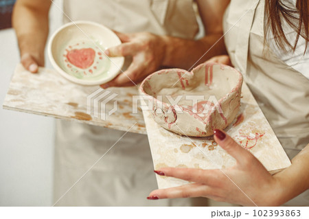 Mutual creative work. Young beautiful couple in casual clothes and aprons. People holds ceramic dishes. Mutual creative work. Young beautiful couple in casual clothes and aprons. People holds ceramic dishes. 102393863