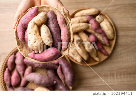 Organic Asian sweet potatoes in basket with hand on wooden background, Table top view Organic Asian sweet potatoes in basket with hand on wooden background, Table top view 102394411
