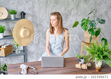 Young female freelancer works on a laptop, responds to messages in social networks. Flower delivery concept. Professional worker in a flower shop. Young female freelancer works on a laptop, responds to messages in social networks. Flower delivery concept. Professional worker in a flower shop. 102396671