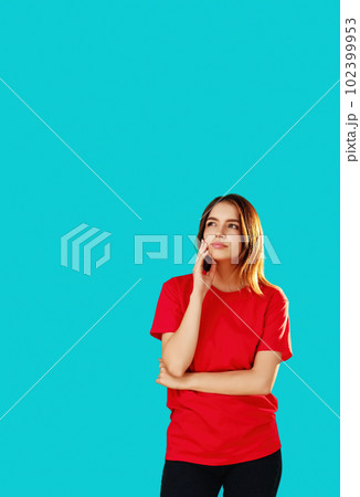 Think over plan. Puzzled woman. Uncertain situation. Beautiful girl in T-shirt holding chin dreaming looking away cunning expression isolated on cyan blue empty space background. 102399953