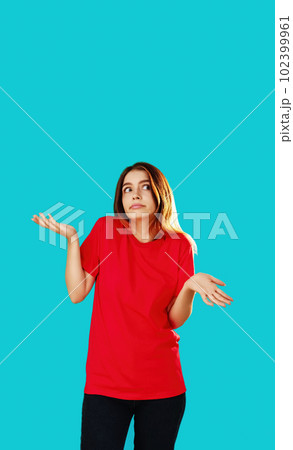 Whatever gesture. Clueless woman. Who knows. Indifferent girl in red T-shirt shrugging shoulders isolated on cyan blue empty space background. Whatever gesture. Clueless woman. Who knows. Indifferent girl in red T-shirt shrugging shoulders isolated on cyan blue empty space background. 102399961