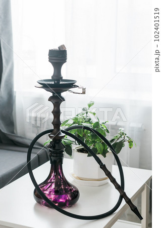 Hookah shisha with glass flask and metal bowl in room background. Traditional Eastern vacation for relaxation 102401519