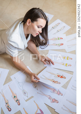 A woman lies on the floor and looks at sketches of swimwear and underwear.  102402342