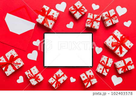 Top view of digital tablet with gift boxes and hearts on colorful background. Tablet with black screen with Holiday decorations gift box top view Top view of digital tablet with gift boxes and hearts on colorful background. Tablet with black screen with Holiday decorations gift box top view 102403578