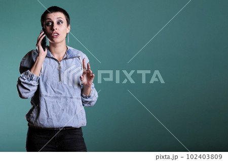 Attractive cheerful woman smiling while having mobile phone conversation with remote friend in studio. Happy female enjoying smarphone discussion standing over isolated background 102403809