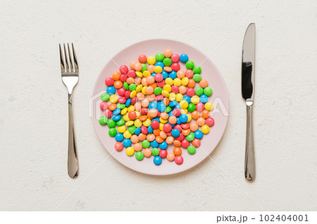cutlery on table and sweet plate of candy. Health and obesity concept, top view on colored background cutlery on table and sweet plate of candy. Health and obesity concept, top view on colored background 102404001