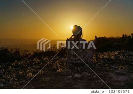 Woman tourist on top of sunrise mountain. The girl salutes the sun, wearing a jacket, white hat and white jeans. Conceptual design. 102405671
