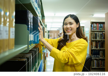 Attractive asian student woman taking textbook from shelf for studying in library. Education, learning and youth lifestyle concept 102406116