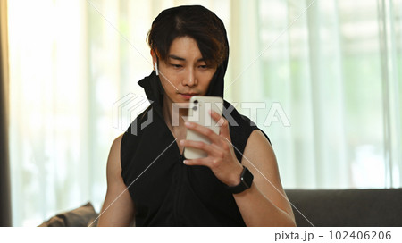 Young sporty fitness man sitting on couch and using smartphone during workout break 102406206