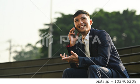 Millennial businessman talking on mobile phone while sitting on stairs in front of office building Millennial businessman talking on mobile phone while sitting on stairs in front of office building 102406208
