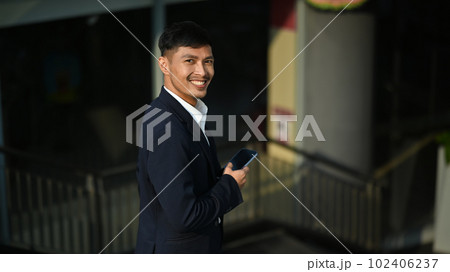 Portrait of smiling young entrepreneur in black suit walking down stairs in office building Portrait of smiling young entrepreneur in black suit walking down stairs in office building 102406237
