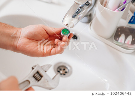 A plumber cleans a water purification filter in faucet faucets in a washbasin A plumber cleans a water purification filter in faucet faucets in a washbasin 102406442