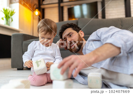 Bearded father playing with toddler child on floor with cubes. 102407669