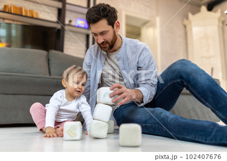 Bearded father playing with toddler child on floor with cubes. 102407676