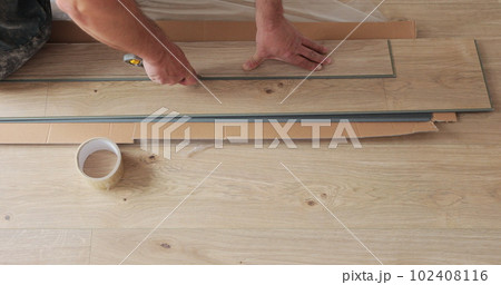 Man with a pencil measures a board before installation, laying laminate during repair. 102408116
